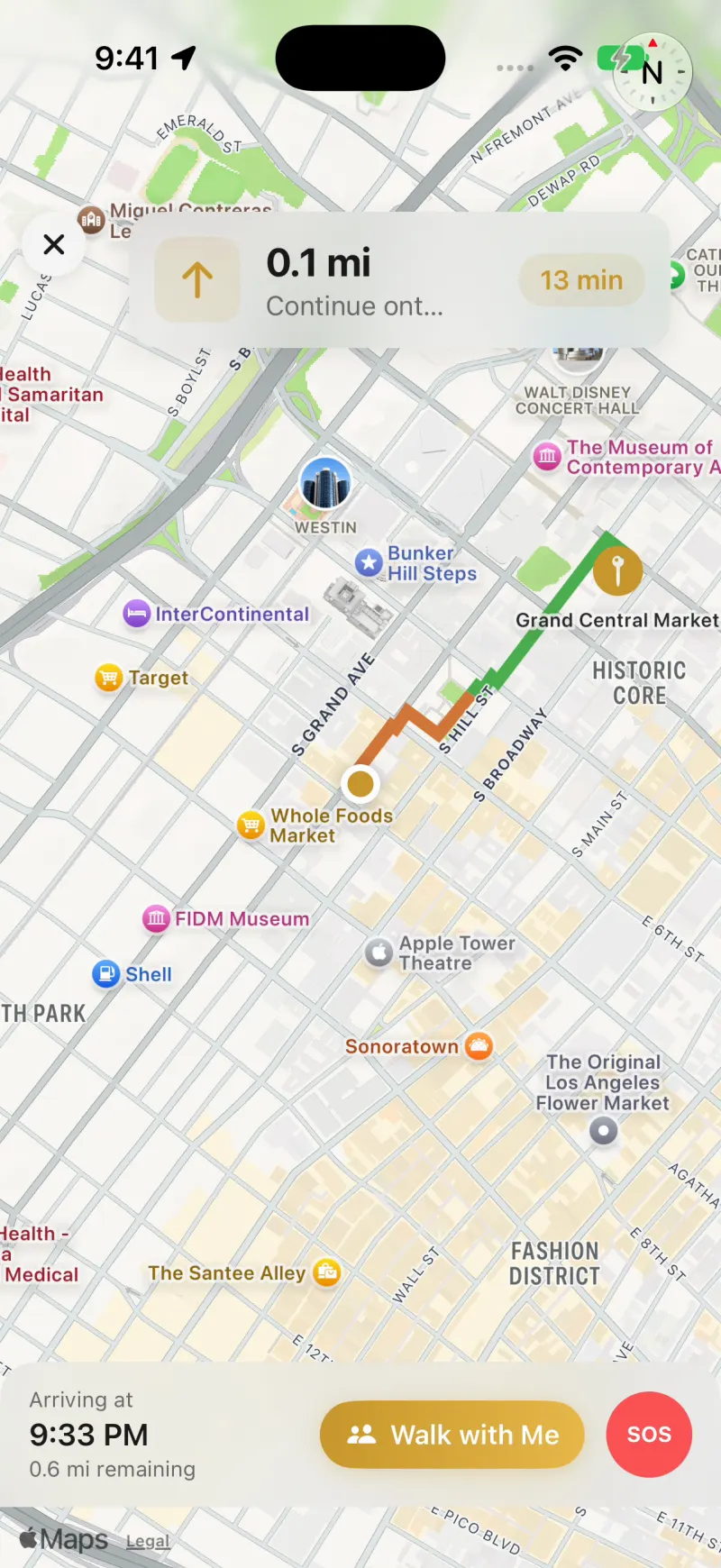 Turn-by-turn navigation on a map of downtown Los Angeles, with the route drawn in green and orange and Walk with Me and SOS buttons at the bottom
